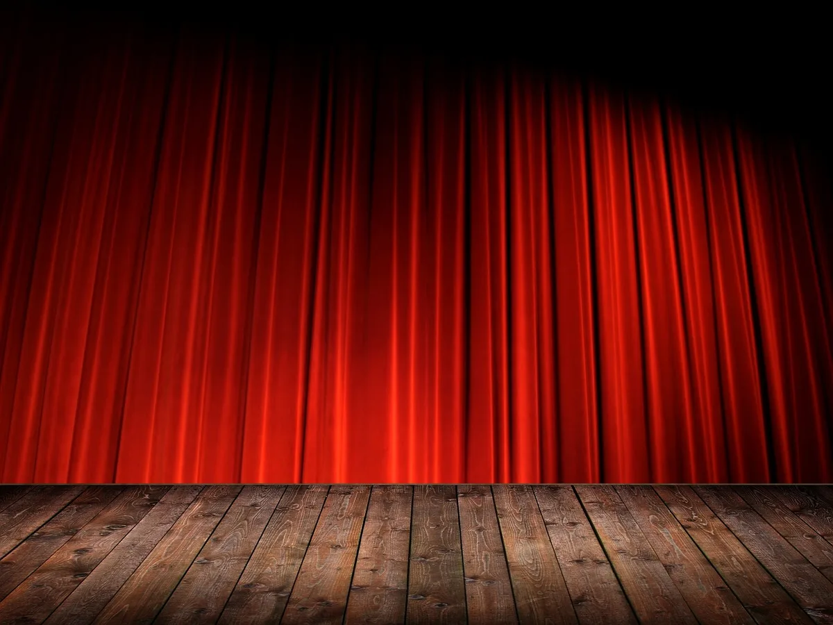 a midshot of an empty cinema auditorium with a single spotlight on the screen and a rolled production schedule on a seat, suggesting upcoming releases